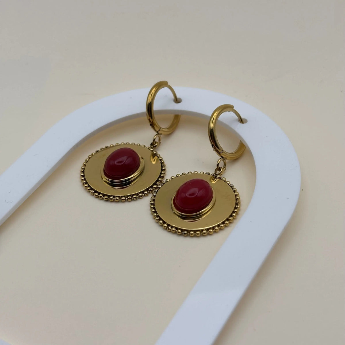 Une paire de boucles d'oreilles dorée pendantes avec cercle dorée et pierre façon camé rouge