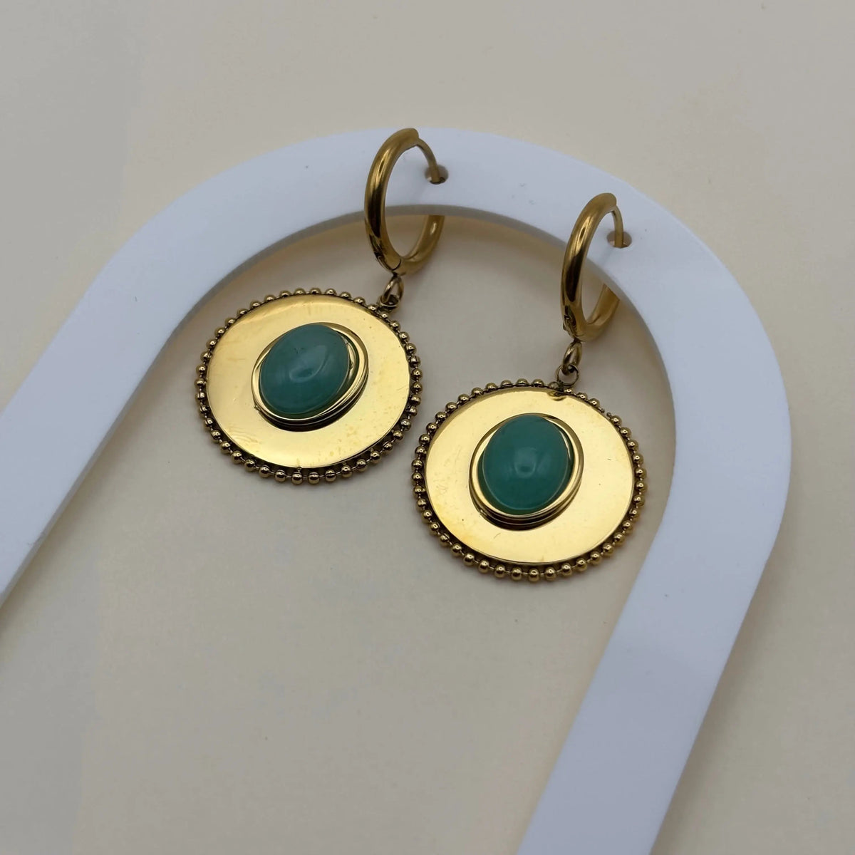 Une paire de boucles d'oreilles dorée pendantes avec cercle dorée et pierre façon camé vert