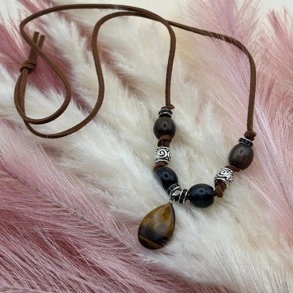 Vue de près d'un collier artisanal sur cordon de cuir brun et pendentif goutte œil de tigre perles verre et acier