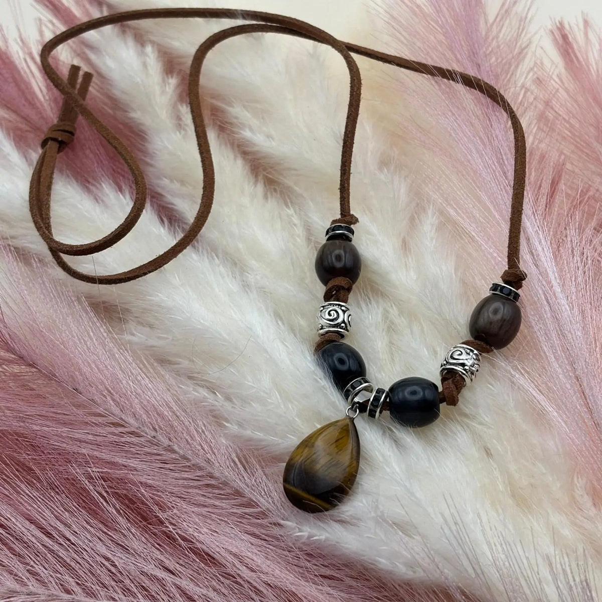 Vue de près d'un collier artisanal sur cordon de cuir brun et pendentif goutte œil de tigre perles verre et acier