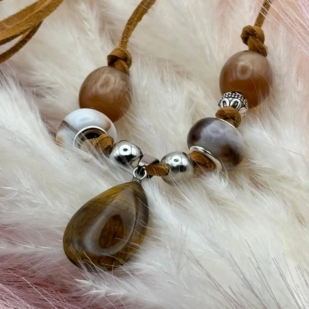 Vue de près d'un collier artisanal avec pendentif œil de tigre sur cordon cuir caramel perles verre et acier Collier artisanal avec pendentif œil de tigre sur cordon cuir caramel perles verre et acier bijou unique