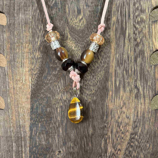 Vue de près d'un collier artisanal sur cordon de cuir saumon avec pendentif goutte œil de tigre et perles de verre et acryliques vendu sur le site internet prêtes à briller