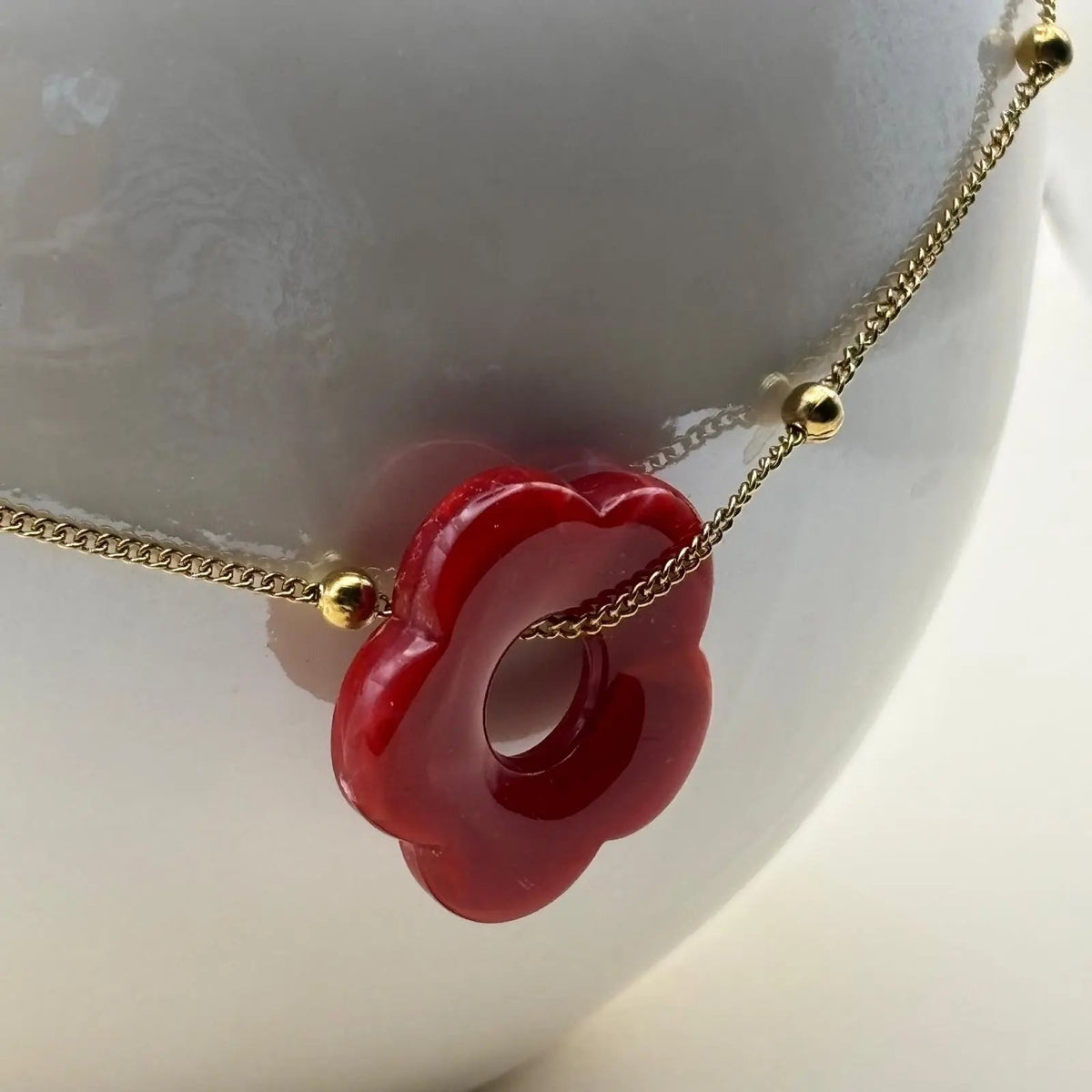Un collier fantaisie avec une chainette dorée et perles dorées un pendentif fleur colorée rouge en acier inoxydable