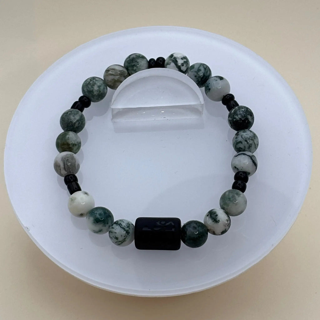 Bracelet aux perles vertes et blanches marbrées rehaussé d’un élément central cylindrique noir gravé