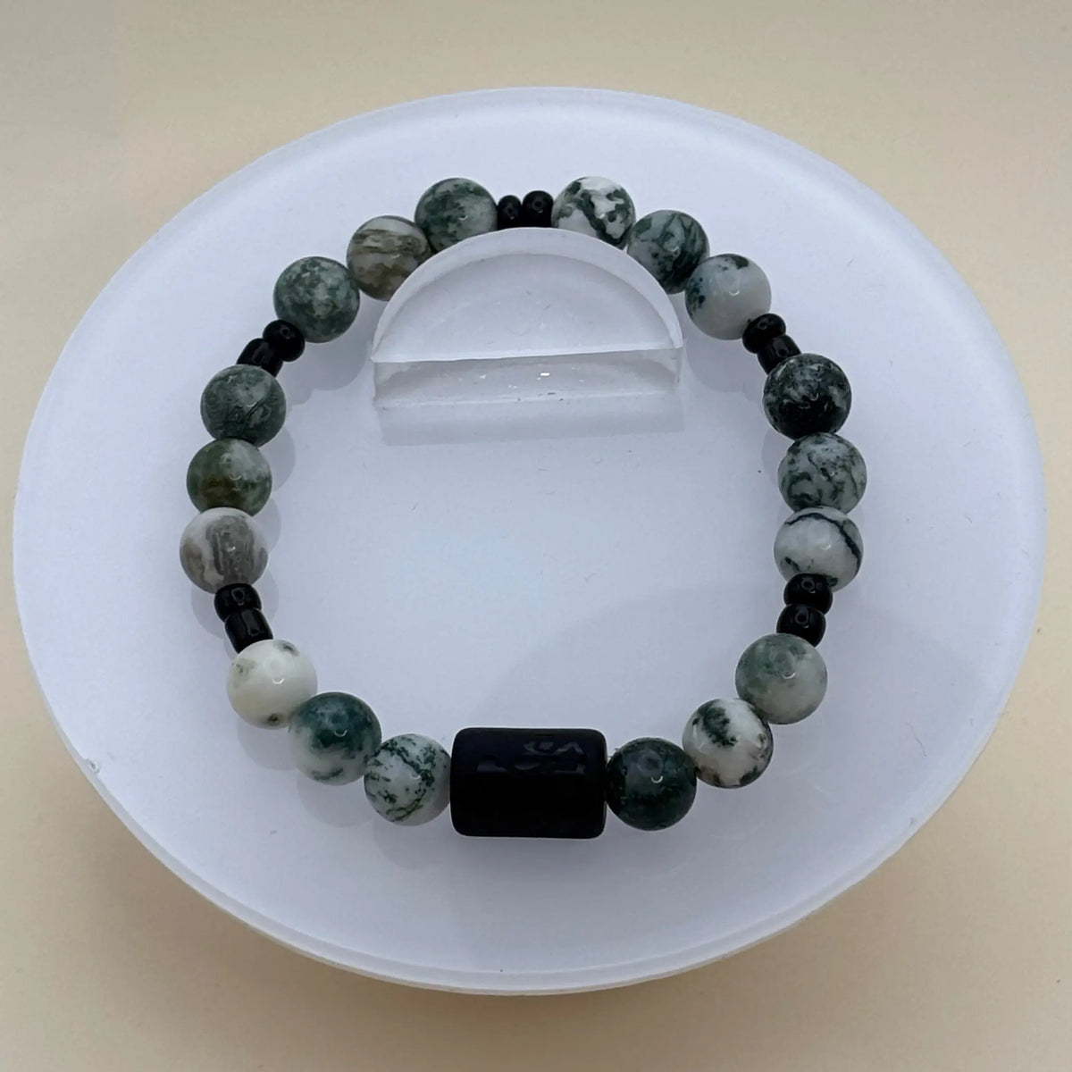 Bracelet aux perles vertes et blanches marbrées rehaussé d’un élément central cylindrique noir gravé