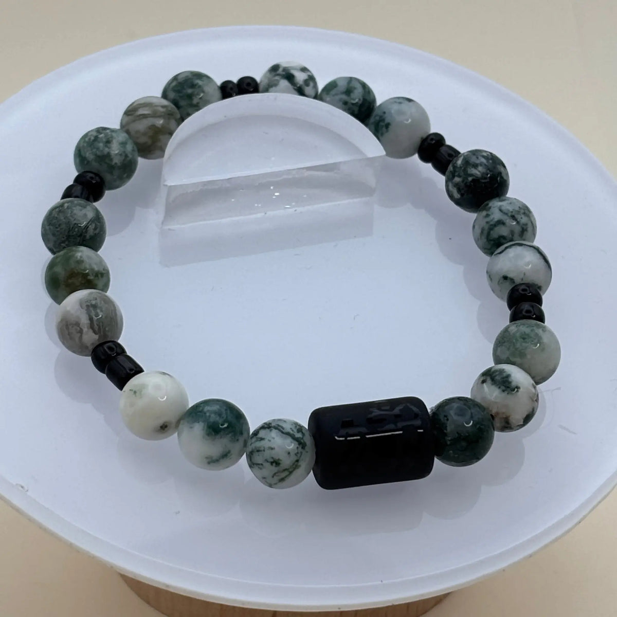 Bracelet aux perles blanches et vertes marbrées souligné par un cylindre noir gravé placé à l’avant