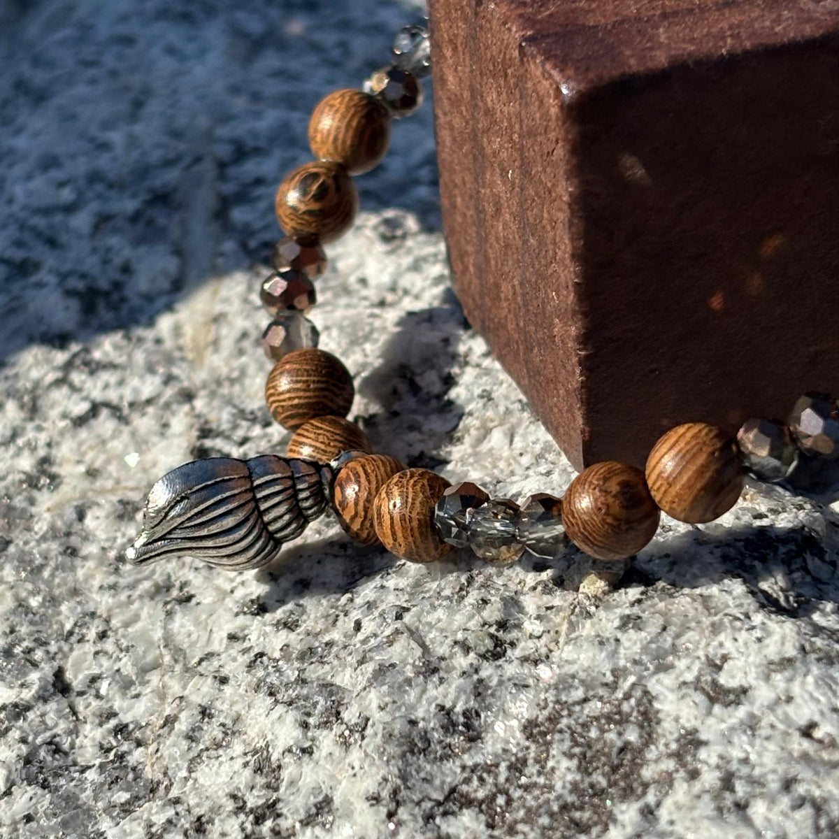 Vue de près d'un bracelet en perles artisanal  avec breloque coquillage argenté et perles en bois sur élastique
