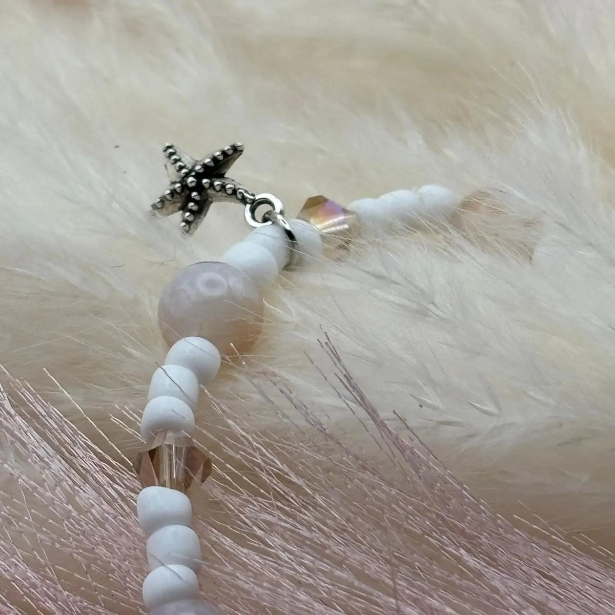 Vue de près d'un bracelet en perles artisanal avec breloques étoiles de mer argentées et perles de verre blanche sur élastique