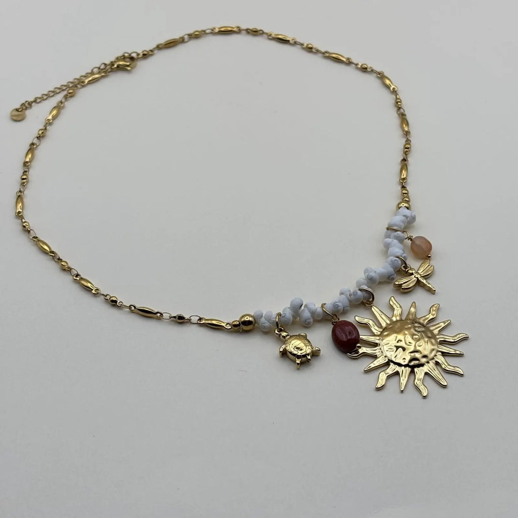 Un collier fantaisie avec un pendentif et breloques soleil perles tortue libellule et petit coquillage de mer blanc