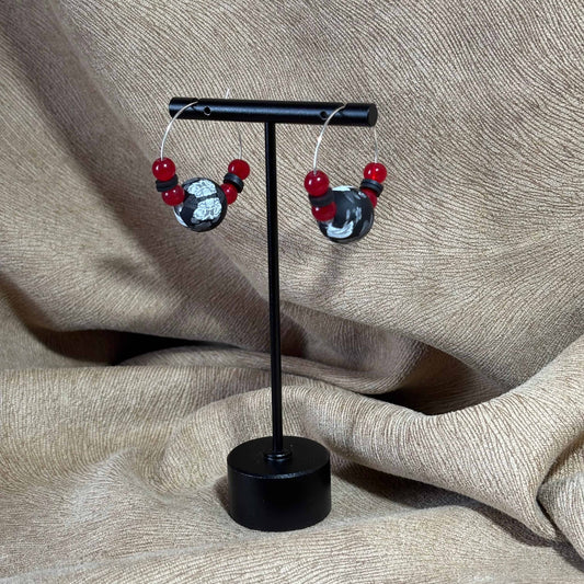 Boucles d'oreilles créoles argentées avec un grosse perle noire et blanche et de petites perles rouges vendues sur le site internet prêtes à briller
