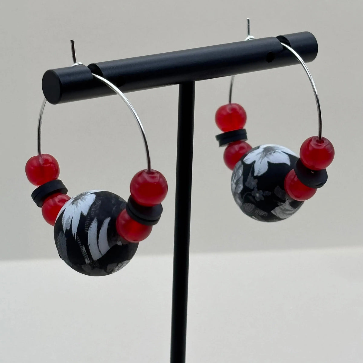 Des boucles d'oreilles créoles argentées avec un grosse perle noire et blanche et de petites perles rouges v