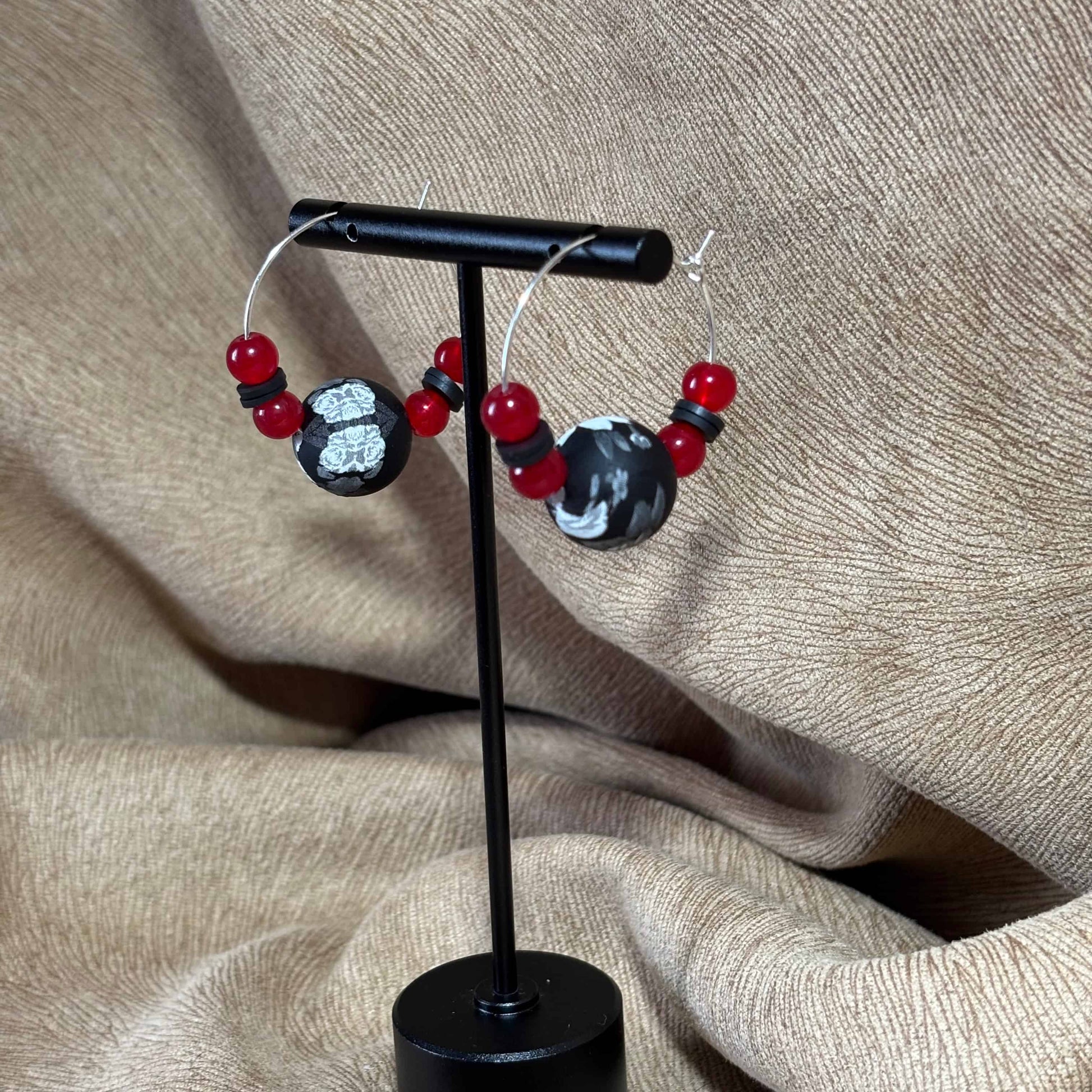 Vue de près de boucles d'oreilles créoles argentées avec un grosse perle noire et blanche et de petites perles rouges vendues sur le site internet prêtes à briller