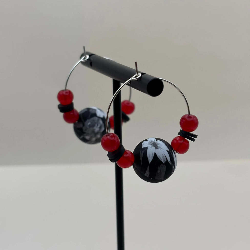 Une paire de boucles d'oreilles créoles argentées avec un grosse perle noire et blanche et de petites perles rouges v