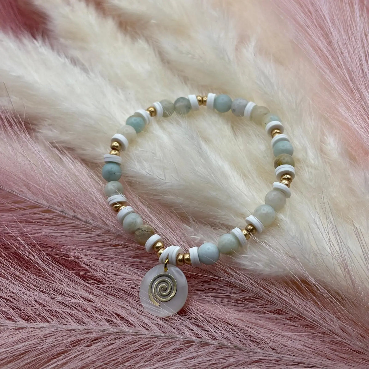 Vue de près d'un bracelet en perles artisanal avec breloque pastille en nacre motif tourbillon et perles naturelles pastels sur élastique