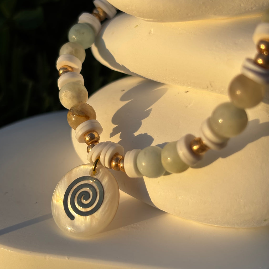 Bracelet en perles artisanal avec une breloque pastille en nacre motif tourbillon et perles naturelles pastels sur élastique