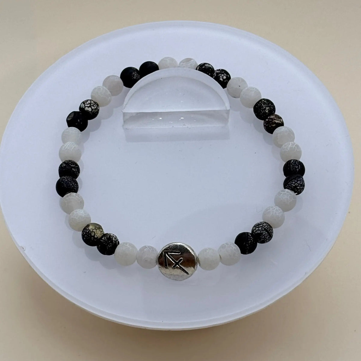 Bracelet alternant perles blanches et noires marbrées avec un médaillon argenté gravé au centre