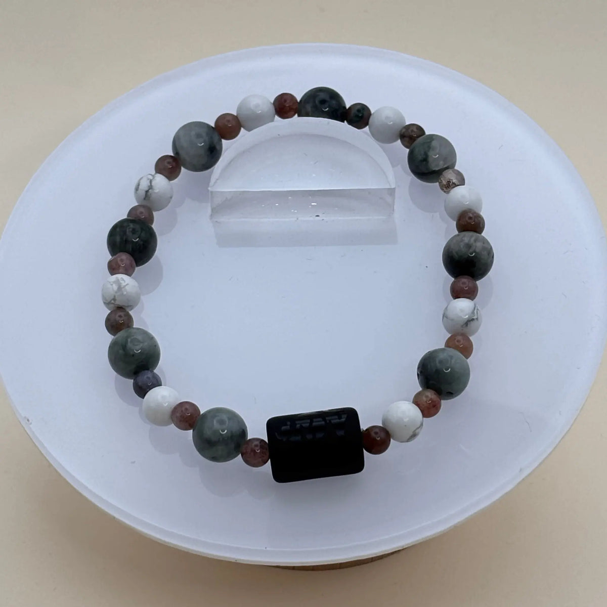 Bracelet composé de perles grises, blanches et brunes réparties harmonieusement autour d’un cylindre noir gravé