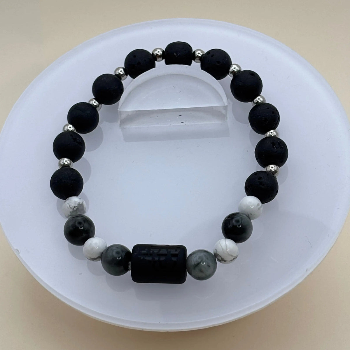 Bracelet associant perles noires et blanches avec un cylindre noir gravé en pièce centrale