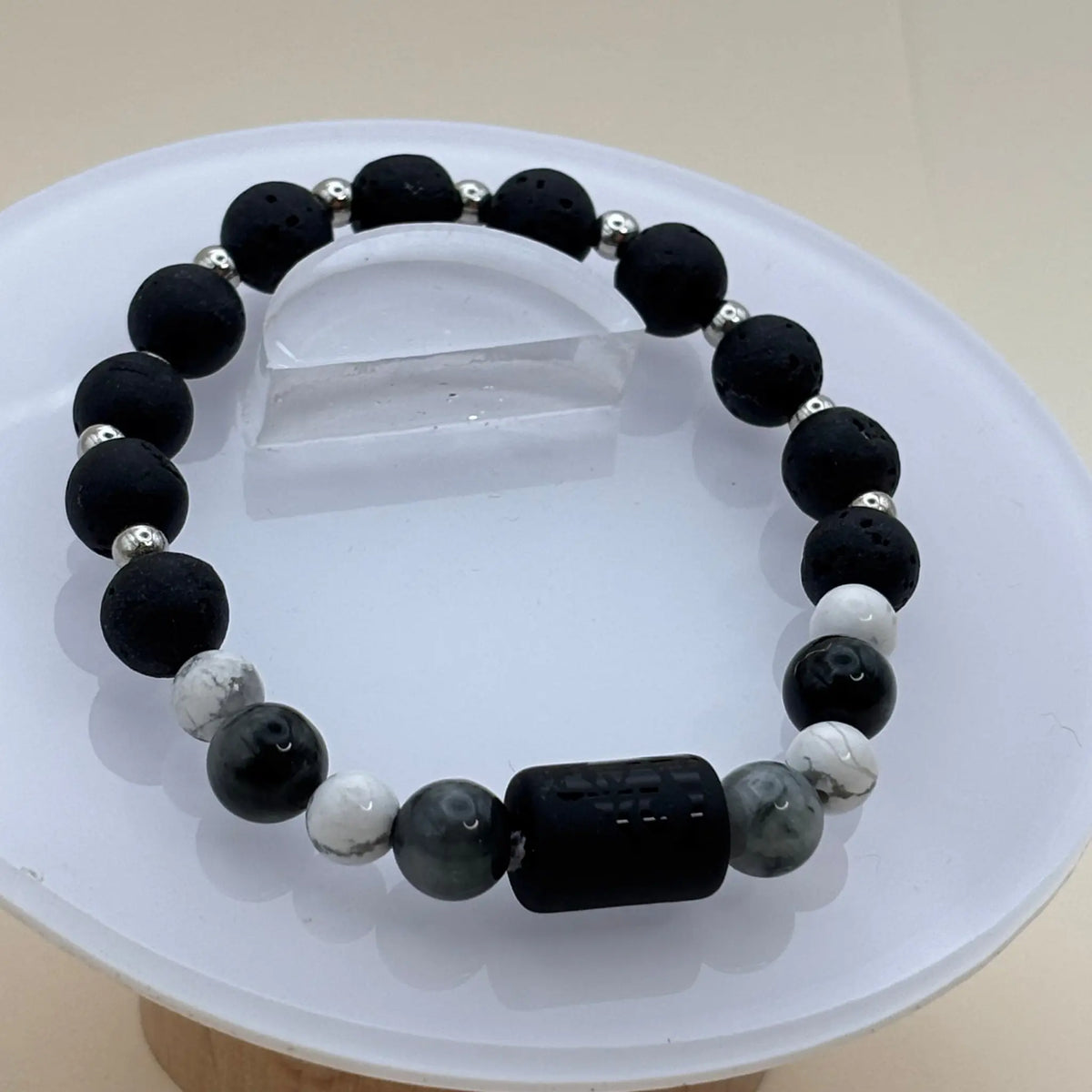 Bracelet mêlant perles noires mates, perles grises et blanches avec un cylindre noir gravé en élément central