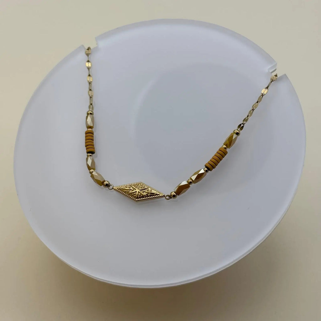 Bracelet doré à mailles fines avec des perles saumon et un motif rose des vents dans un losange