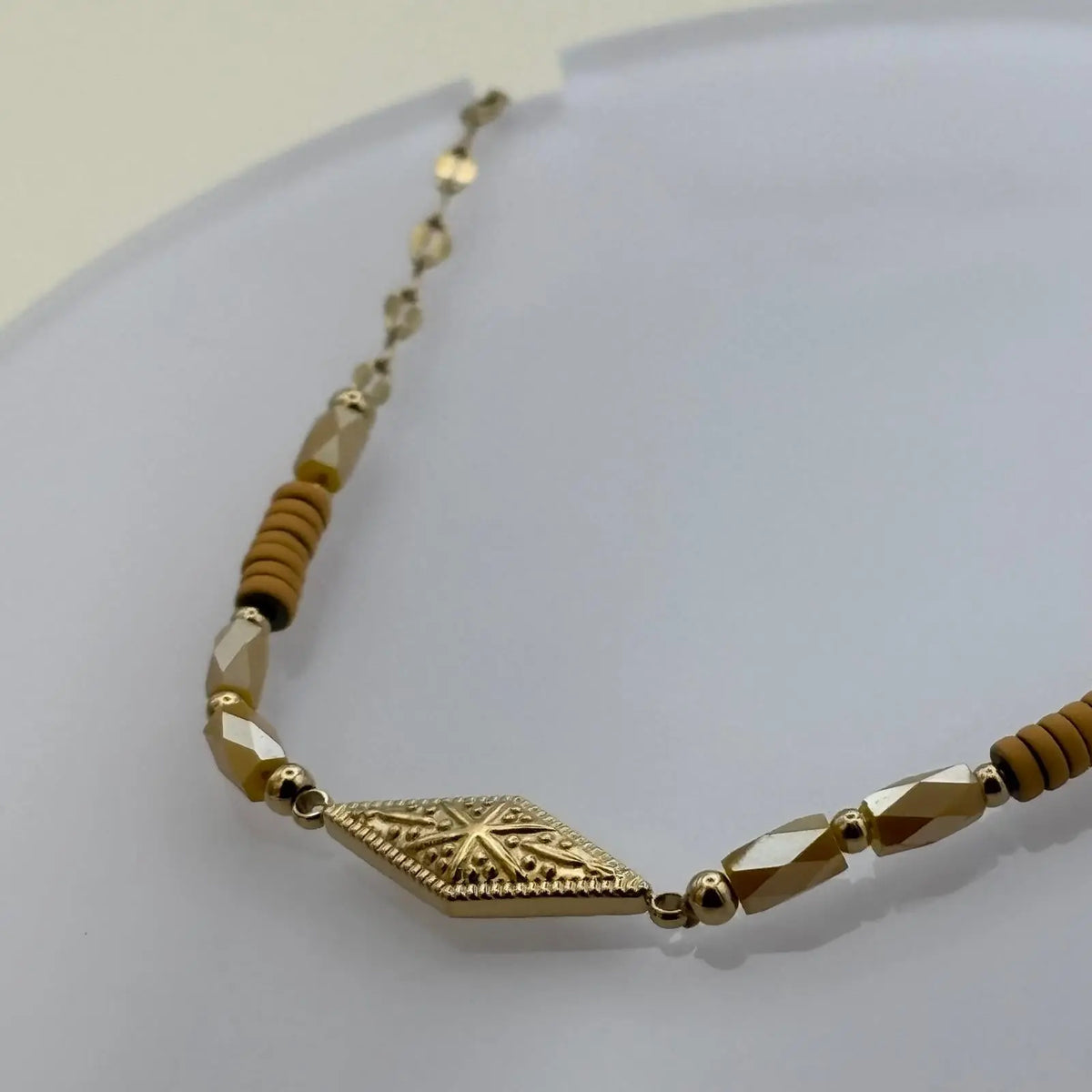 Bracelet doré à mailles fines avec des perles saumon et motif rose des vents dans un losange