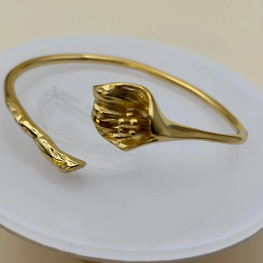 Vue de près d'un bracelet doré rigide ouvert avec un motif fleur d'arum dorée