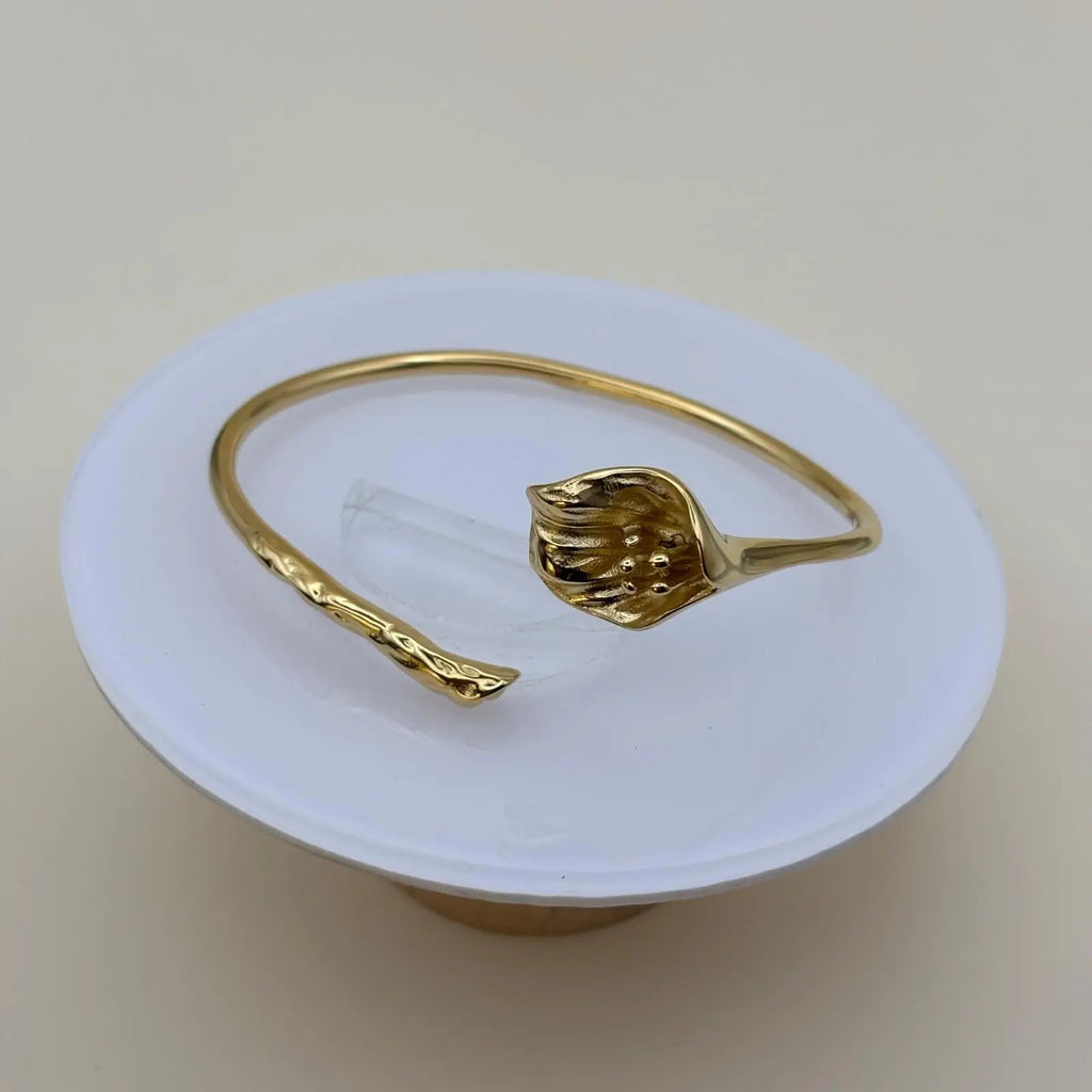 Vue de près d'un bracelet de couleur dorée rigide ouvert avec un motif fleur d'arum dorée