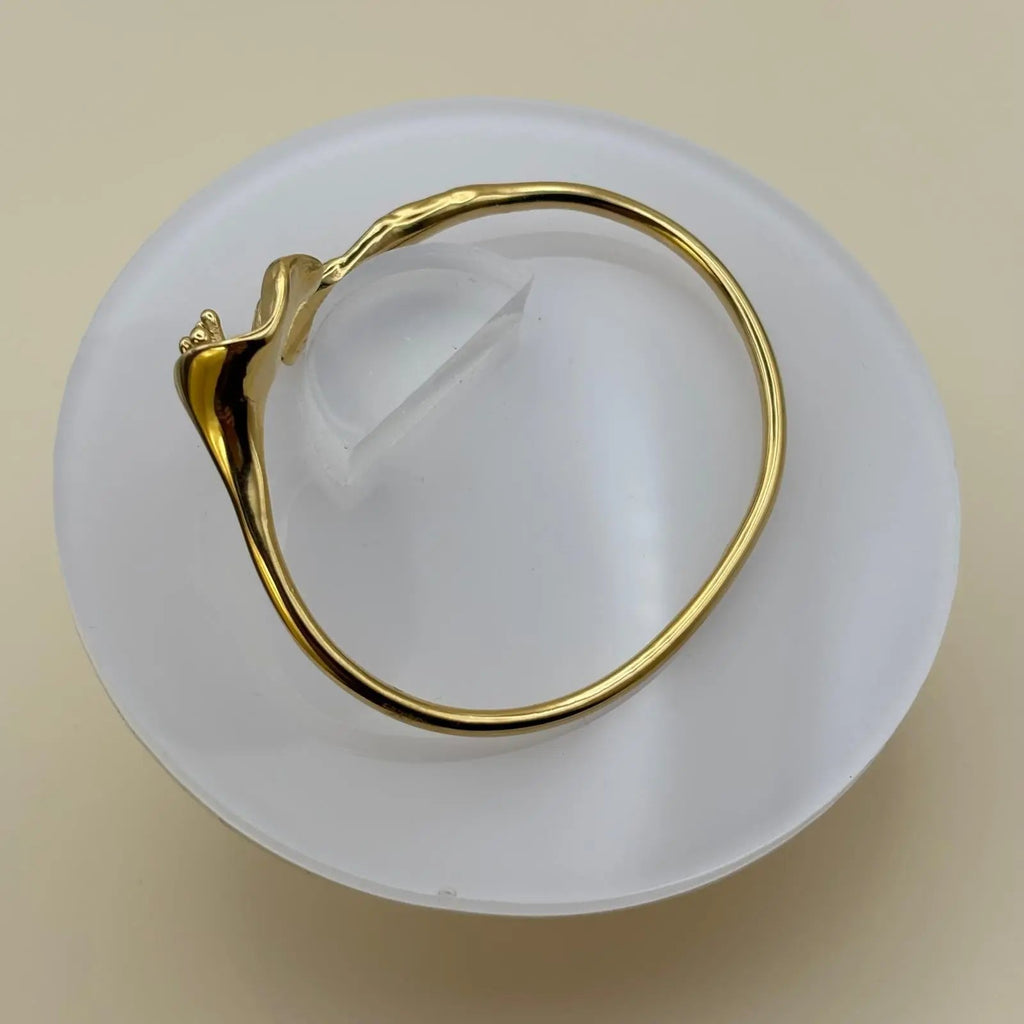 Vue de près d'un bracelet doré rigide ouvert avec le motif d'une fleur d'arum dorée