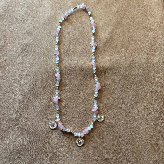 Collier artisanal | Collier avec breloques soleil doré sur fond blanc | Perles de verre blanche et acrylique rose sur élastique