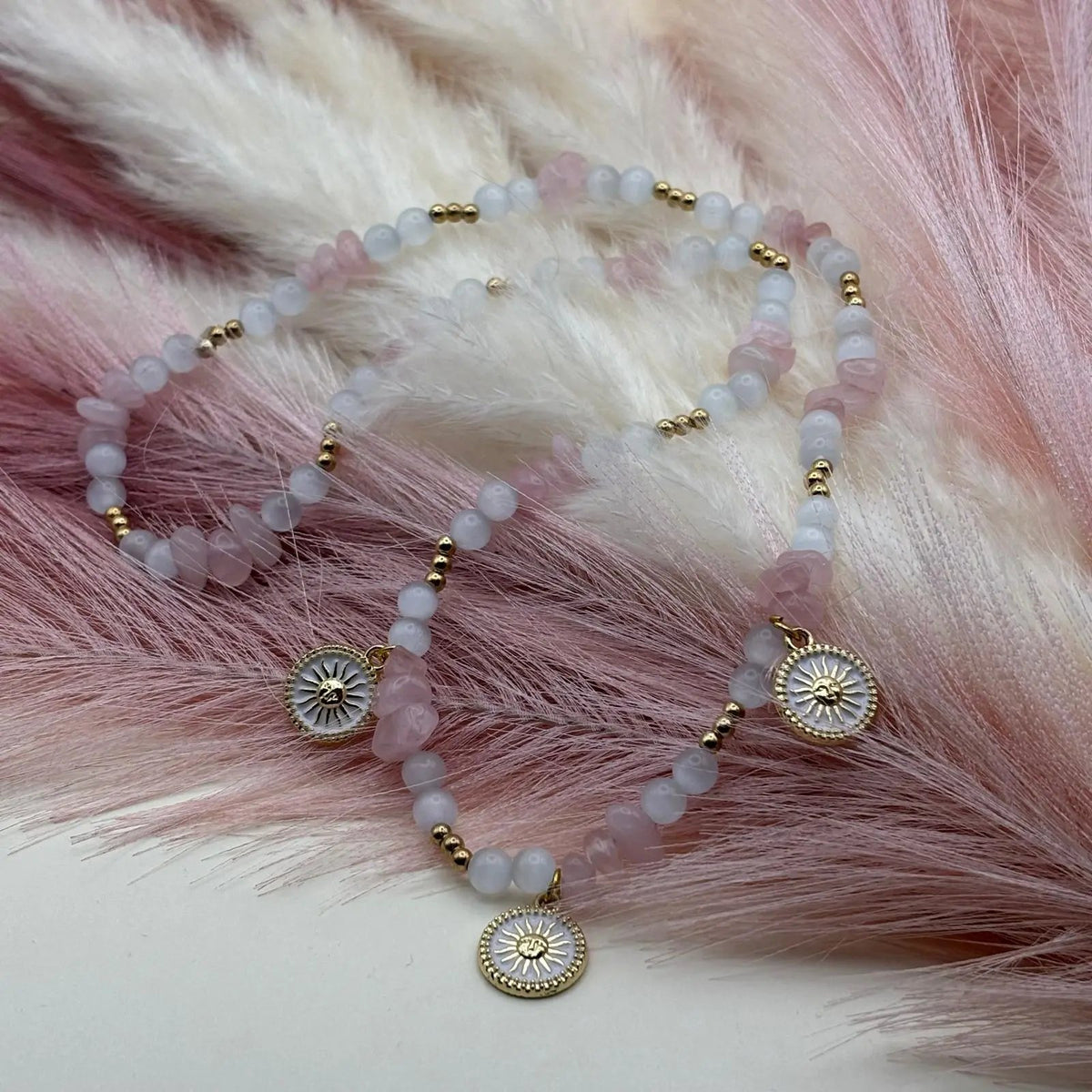 Collier artisanal en perles rose et blanches avec pendentifs décoratifs en forme de soleil