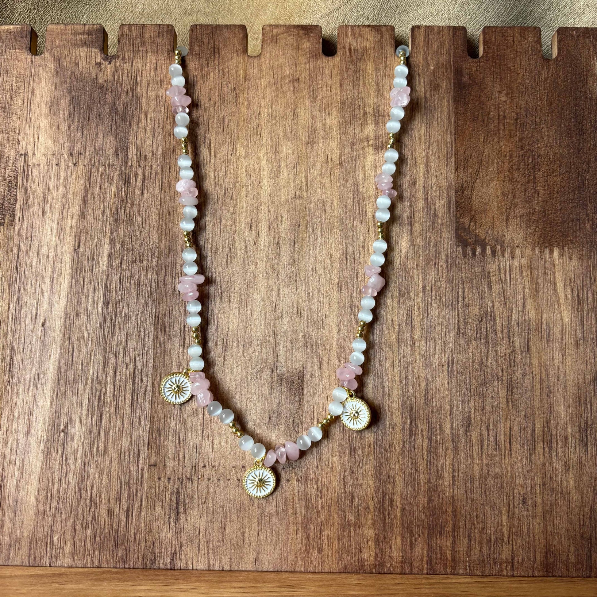 Collier artisanal | Collier avec breloques soleil doré sur fond blanc | Perles de verre blanche et acrylique rose