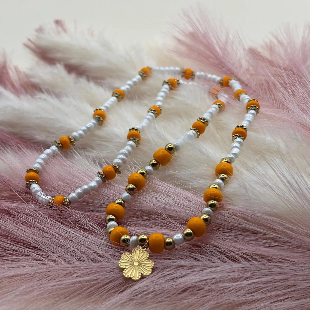 Vue de près d'un collier en perles artisanal avec perles oranges et blanches et pendentif soleil doré