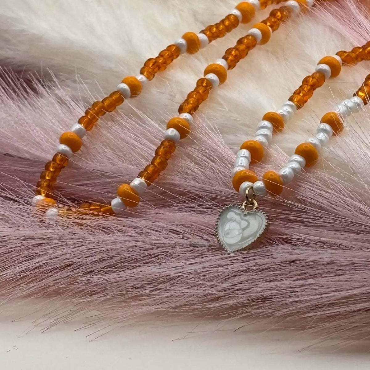Collier artisanal avec des perles orangées et une breloque cœur nacré