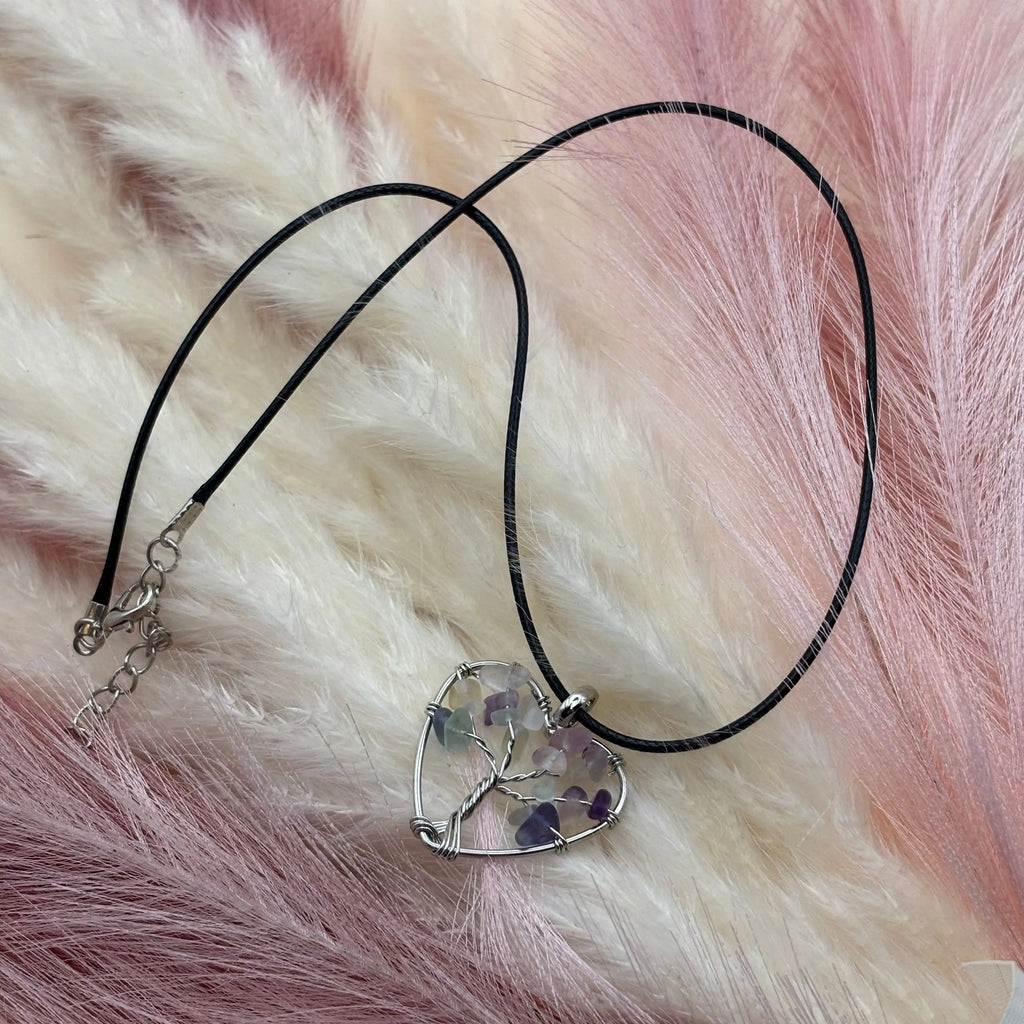 Un pendentif avec cordon noir et un cœur en métal argenté orné de très petites pierres pastels 