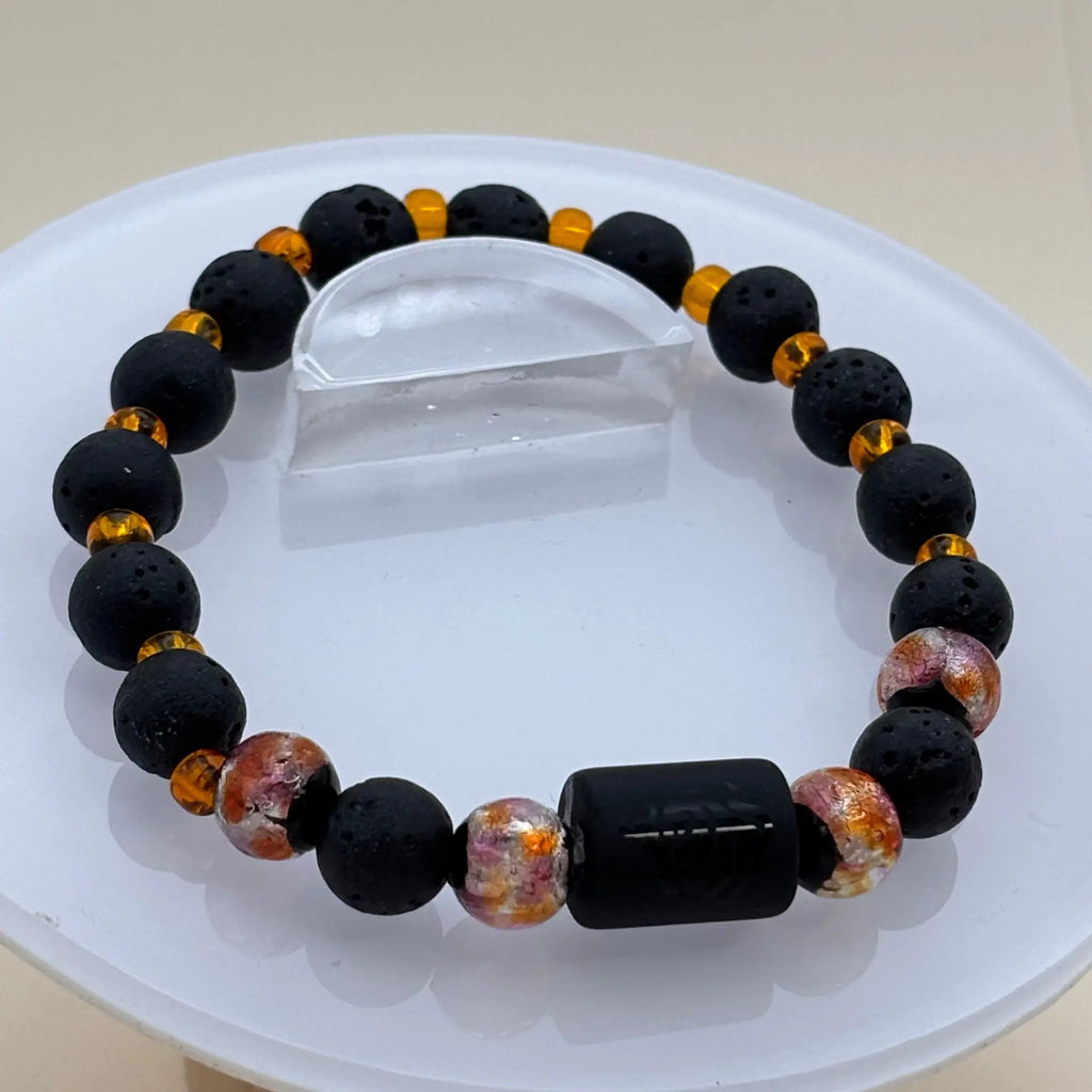 Bracelet alternant perles noires et perles orange translucides accompagné d’un cylindre noir gravé