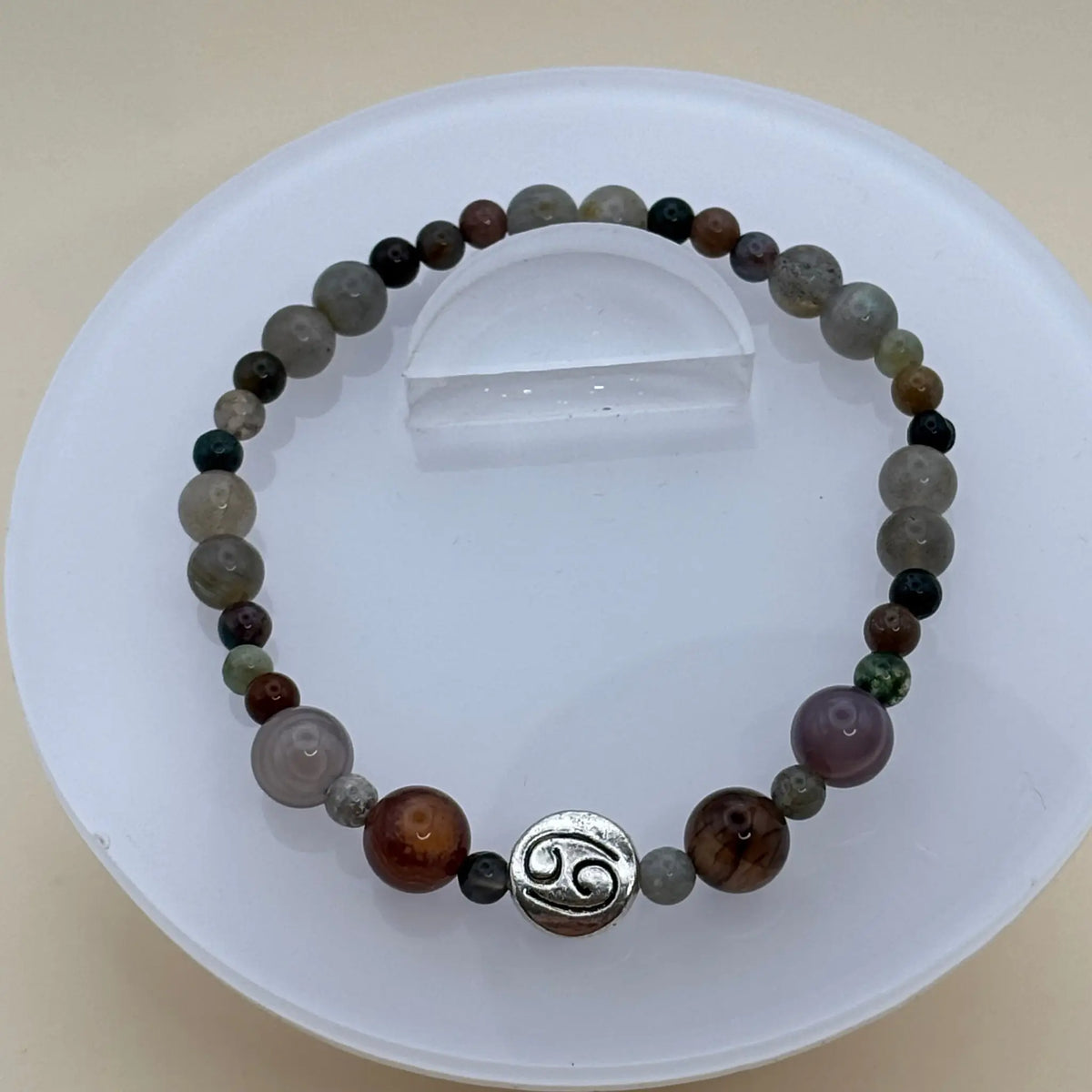 Bracelet aux perles multicolores dans des tons gris et bruns orné d’un médaillon argenté gravé