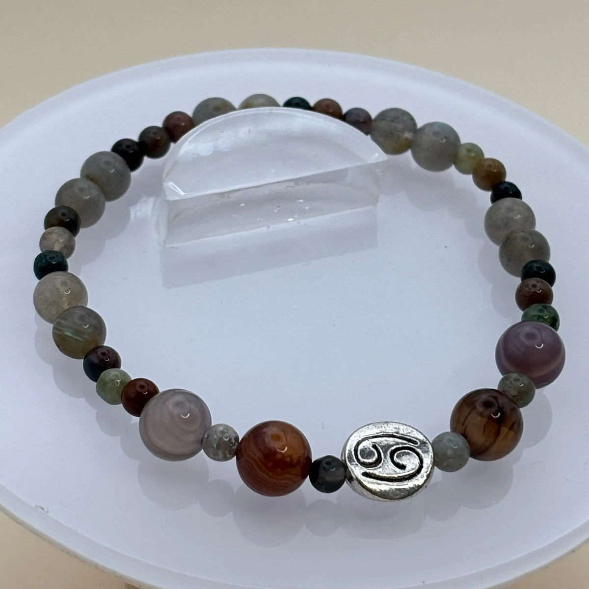 Bracelet aux perles variées gris, beige et brun avec un médaillon argenté gravé placé à l’avant