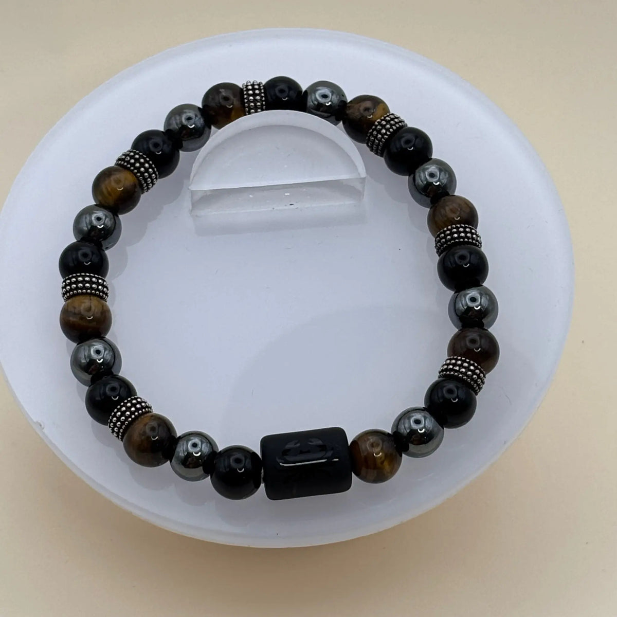 Bracelet combinant perles noires, grises et dorées avec des anneaux métalliques décoratifs et un cylindre noir gravé