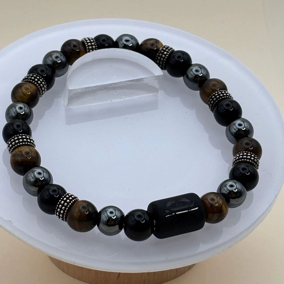 Bracelet composé de perles noires, grises et dorées agrémenté d’anneaux métalliques décoratifs et d’un cylindre noir gravé