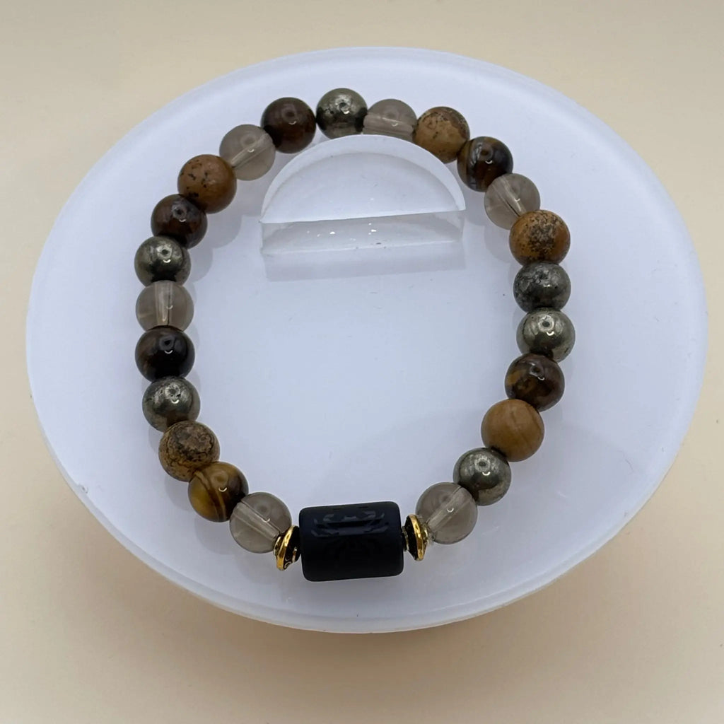 Bracelet aux perles brunes, dorées et transparentes rehaussé d’un cylindre noir gravé entouré d’anneaux dorés