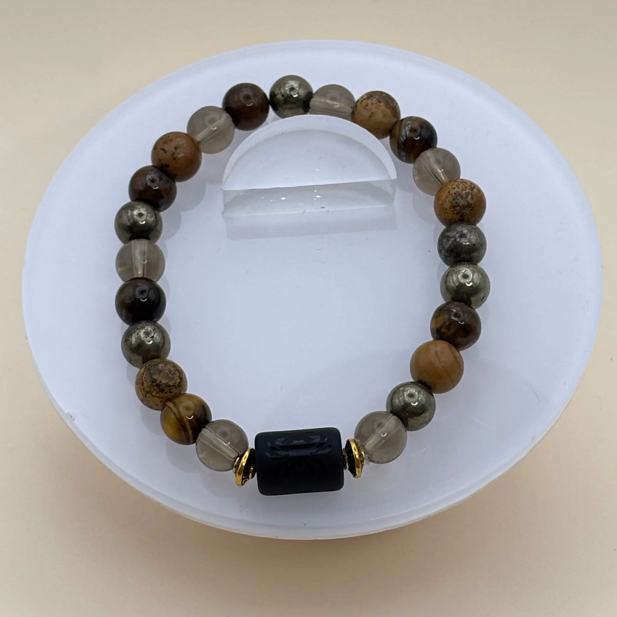 Bracelet aux perles brunes, dorées et transparentes rehaussé d’un cylindre noir gravé entouré d’anneaux dorés