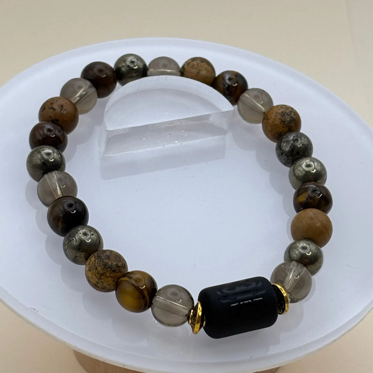 Bracelet formé de perles brunes, dorées et transparentes avec un cylindre noir gravé entouré d’anneaux dorés